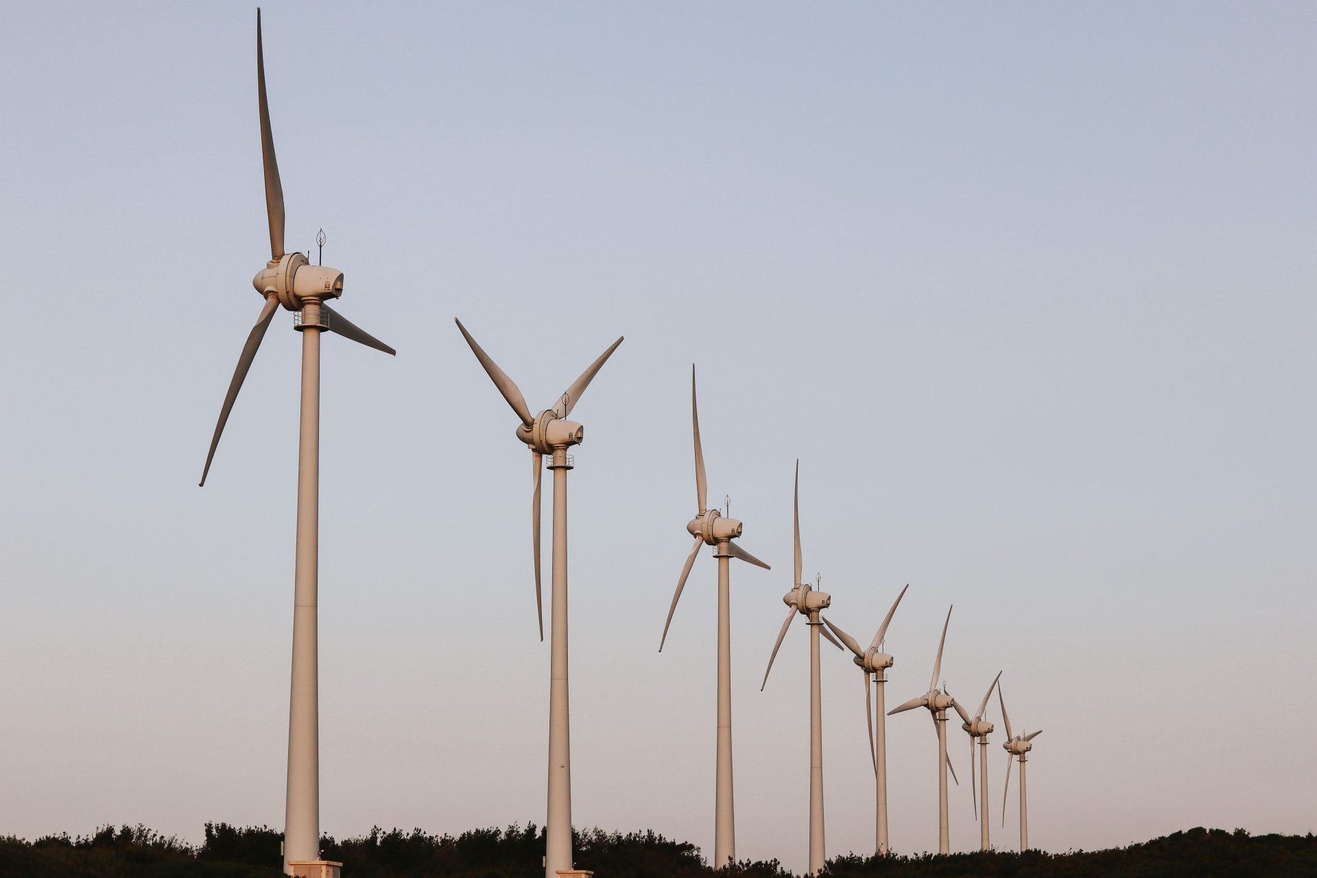 Eine Reihe von Windkraftanlagen steht unter einem klaren blauen Himmel aufgereiht und gewinnt erneuerbare Energie.