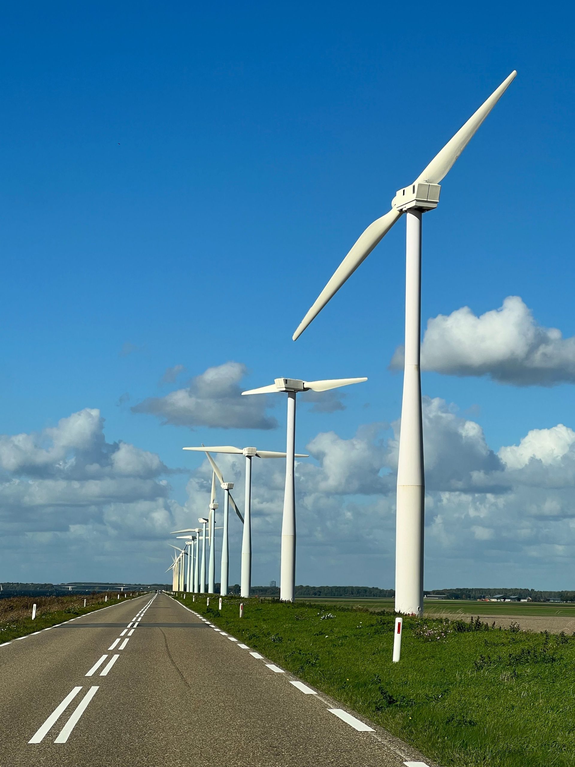 Malerischer Blick auf Windkraftanlagen entlang einer leeren Straße unter blauem Himmel in FL, Niederlande.