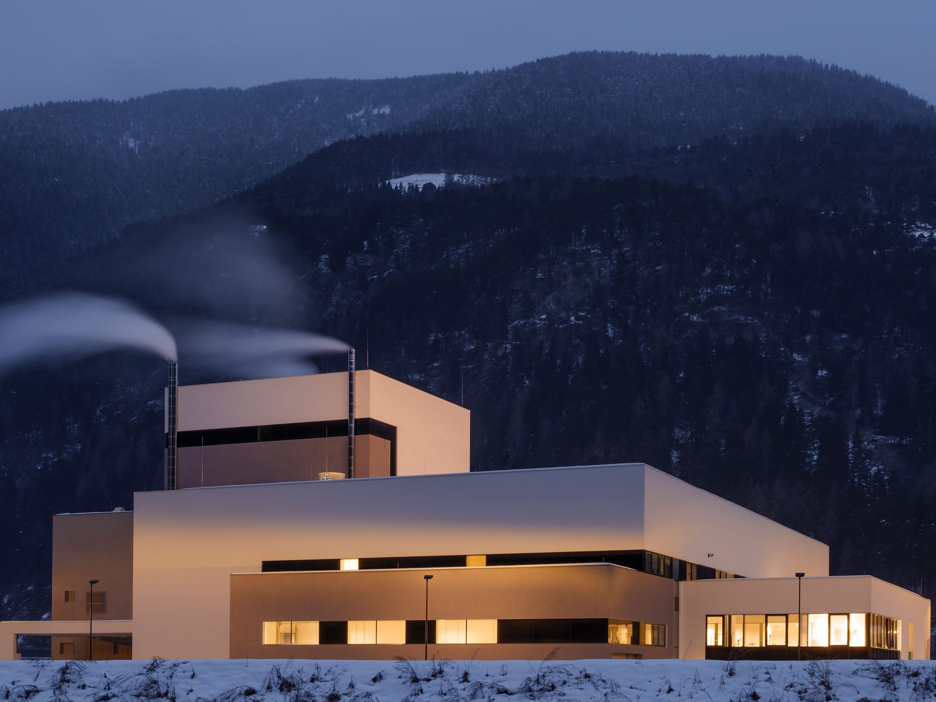 Modernes Gebäude, eingerahmt von schneebedeckten Bergen in Trentino-Südtirol während der Abenddämmerung.