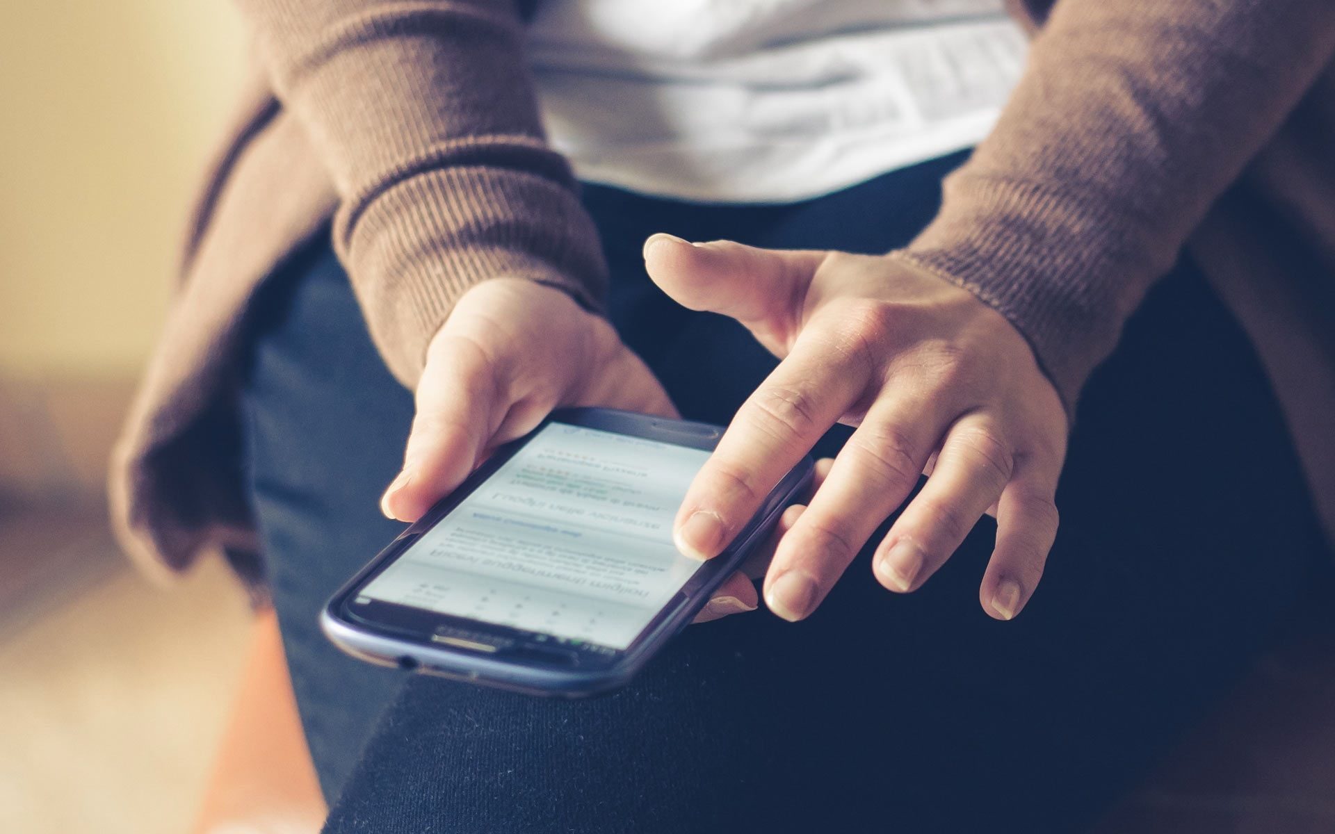 Nahaufnahme eines Erwachsenen, der in Innenräumen ein Smartphone benutzt und im Internet surft, wobei der Fokus auf dem Bildschirm liegt.
