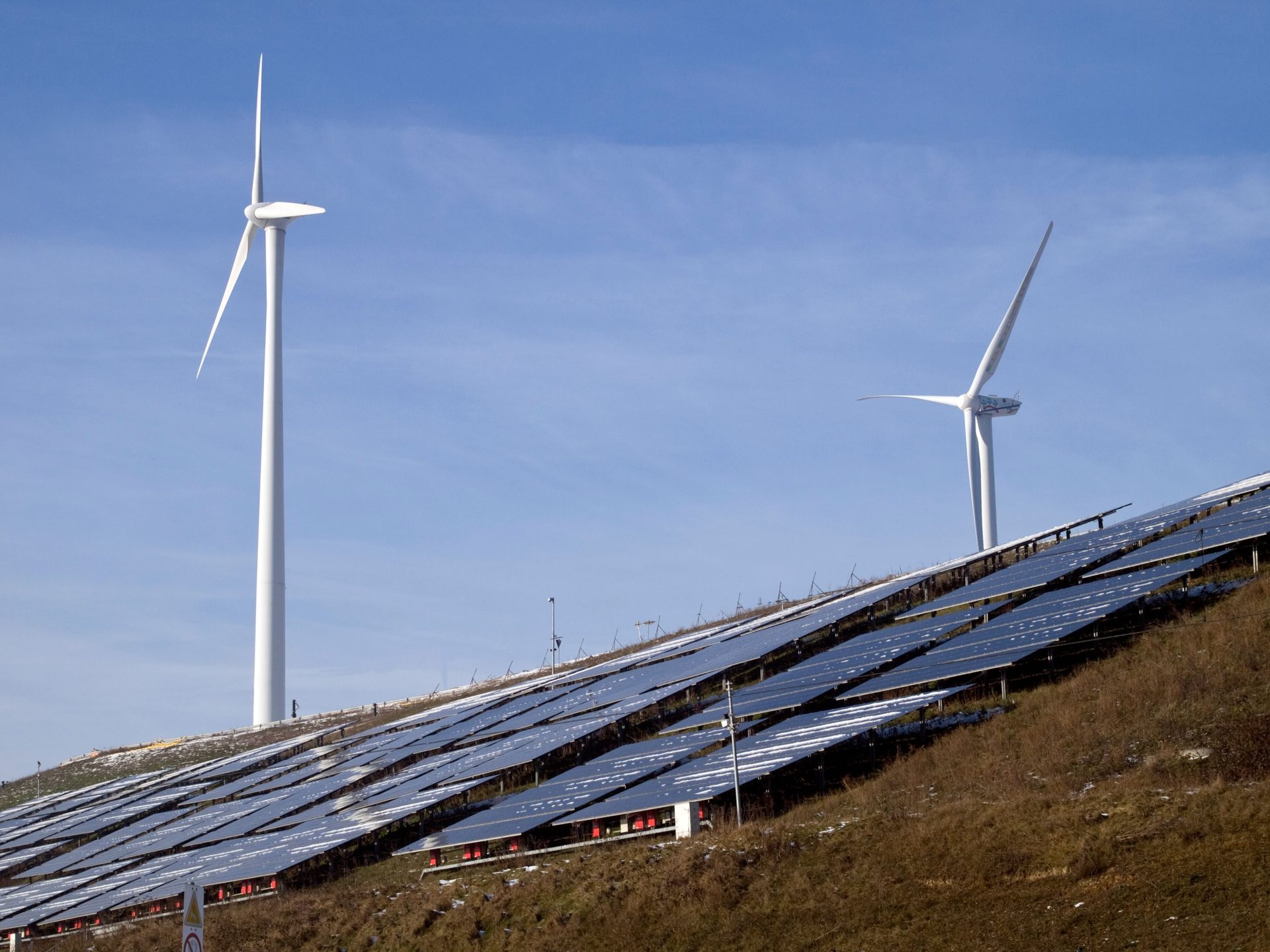 Windkraftanlagen und Solarmodule an einem Hang, die unter klarem Himmel erneuerbare Energie gewinnen.