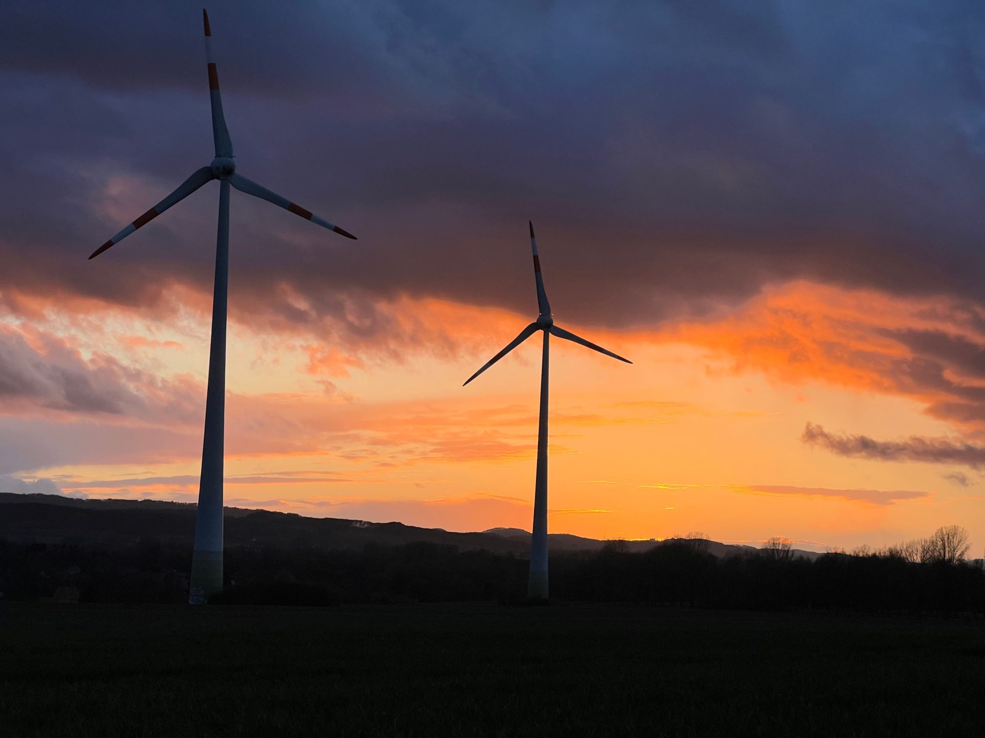 Als Silhouetten vor einem farbenprächtigen Sonnenuntergang im ländlichen Deutschland dargestellte Windkraftanlagen, die erneuerbare Energien veranschaulichen.