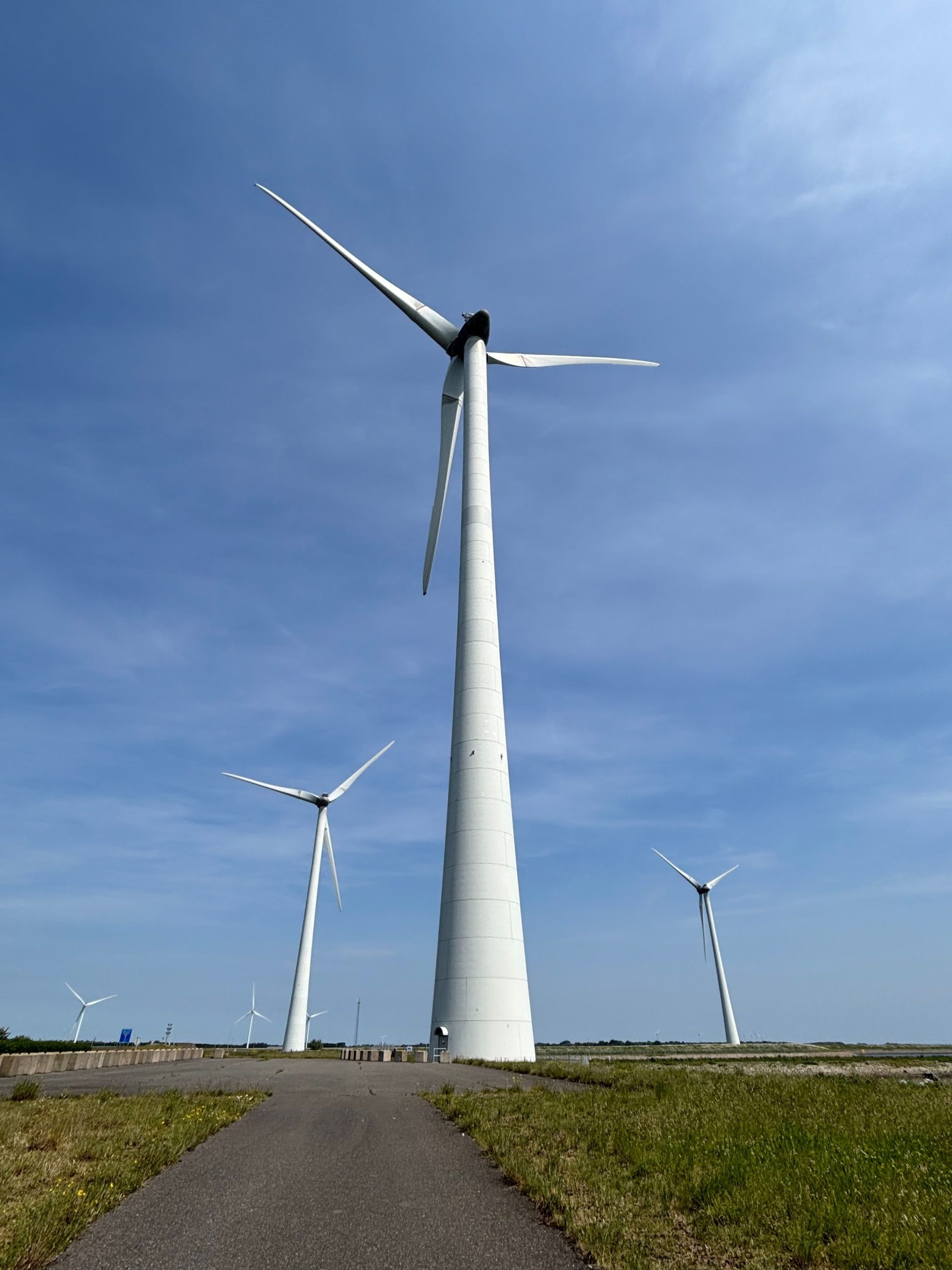 Drei große Windkraftanlagen auf einer offenen Grasfläche unter einem hellen, klaren Himmel, die erneuerbare Energien und Nachhaltigkeit symbolisieren.