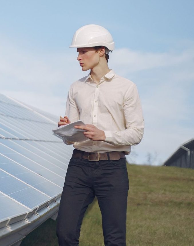 Junger, ernsthafter Ingenieur in formeller Kleidung und mit Helm erstattet während der Inspektion eines Solarparks Bericht.