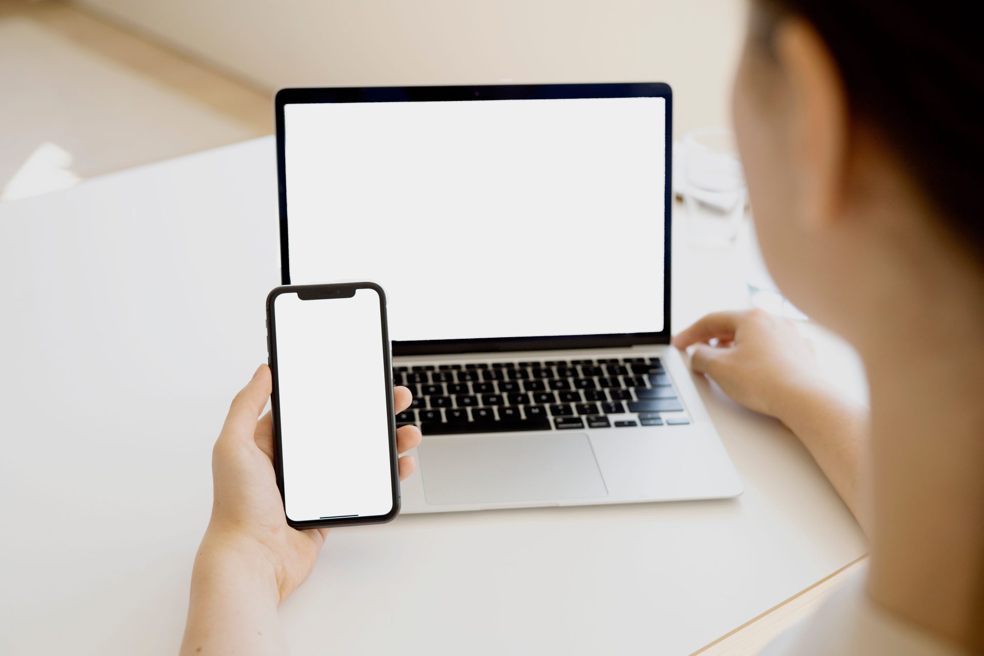 Eine Frau hält ein Smartphone vor einen Laptop und schafft so eine nahtlose technologische Umgebung.
